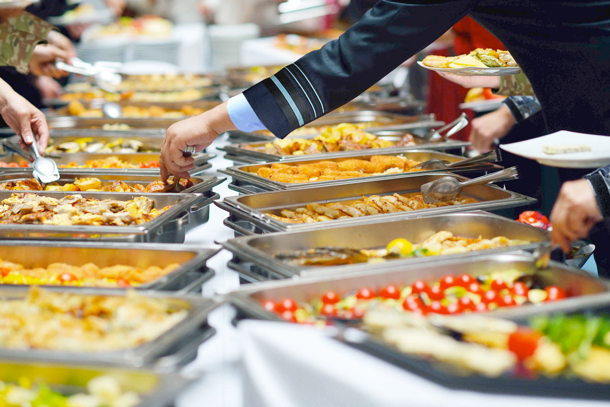 People serving themselves food from a large buffet spread at a catered event.