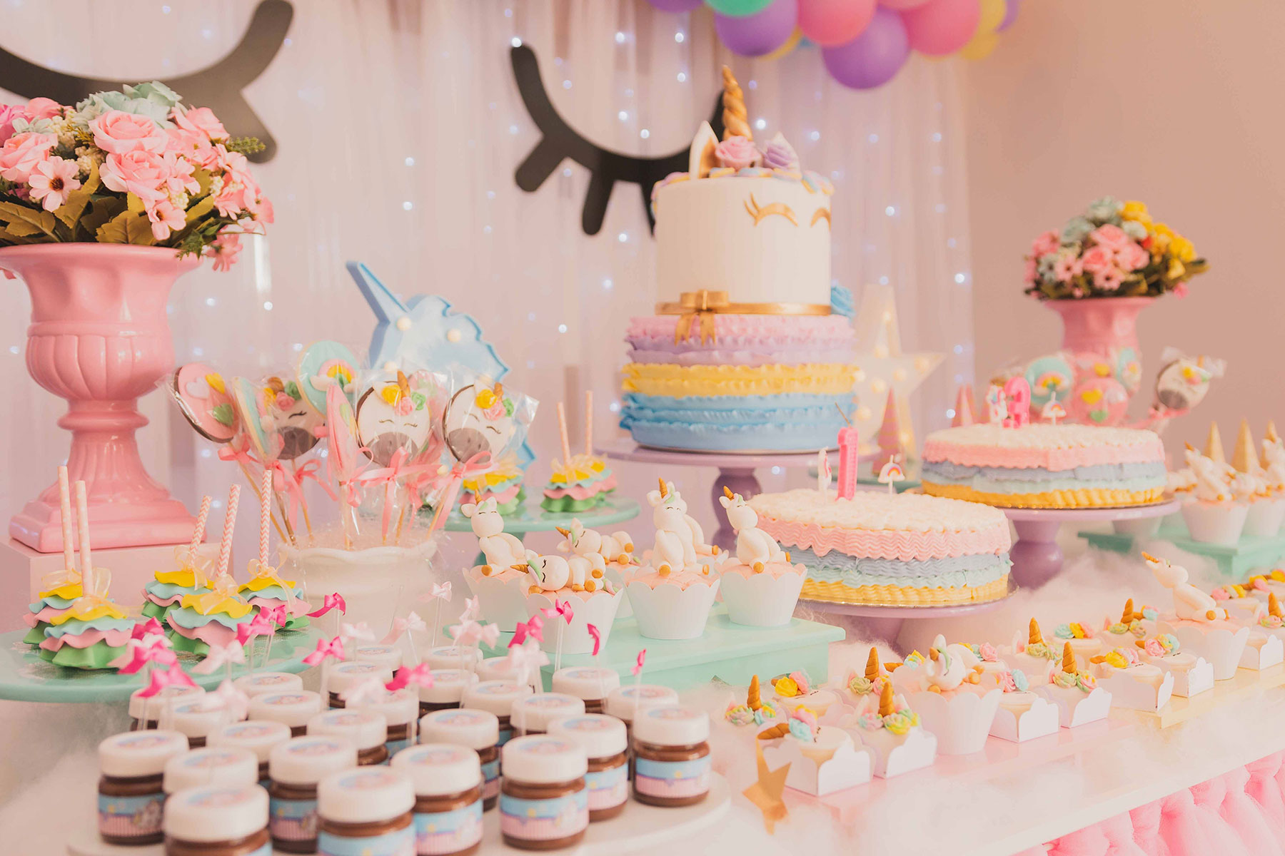 A beautifully decorated dessert table at a unicorn-themed party, featuring a multi-tiered cake, cupcakes, cake pops, and other sweets in pastel colors.